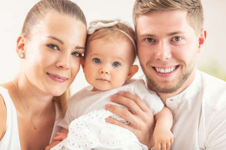 Happy young family with mother, father and baby daughter all smiling into the camera.