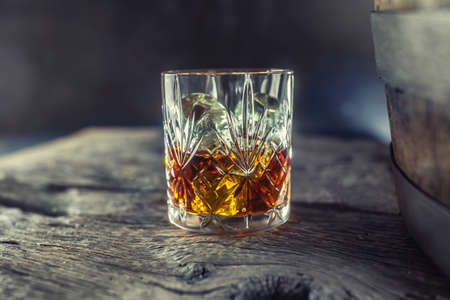 Glass with whiskey rum brandy or bourbon on an old table near a wooden barrel.の写真素材