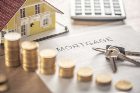 Mortgage contract for the purchase or sale of an apartment house or real estate. Work desk with contract coins model house calculator and pen.の写真素材