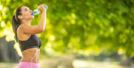 Young sporty woman drinking water from a bottle after exercising at the park.