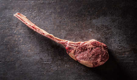 Raw tomahawk steak on a old rustic board - Top of view.