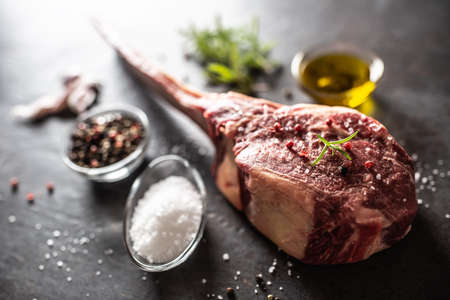 Raw tomahawk steak with salt spices garlic and herbs on a old rustic board.