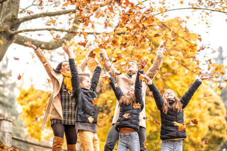 Children throwing colorful leaves up in the air with their parents outdoors during fall.の写真素材