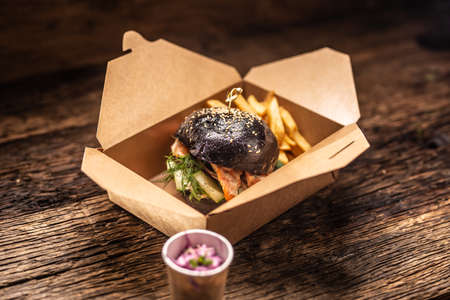 Tasty black burger takeaway in a box of recycled paper on wooden board.の写真素材