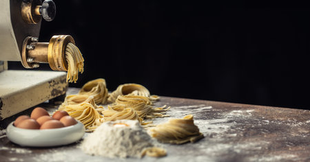 Flour, eggs and a pasta maker producing fresh Italian fettuccine with a dark background.の写真素材