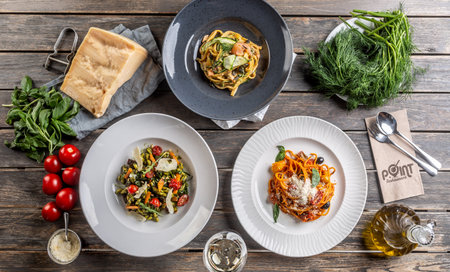 Top view of various pasta dishes served on plates, surrounded by ingredients on a vintage wooden surface.の写真素材