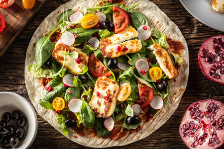Top view of an open top vegetarian tortilla with salad, radish, cherry tomatoes, olives, pomegranate...