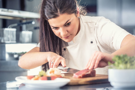 Professional female sushi chef cuts tuna fish in a pro kitchen.の写真素材
