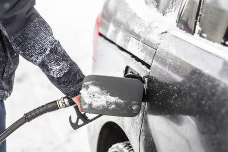 An open fuel tank with gas pistol in it held my a male in snowy winter.