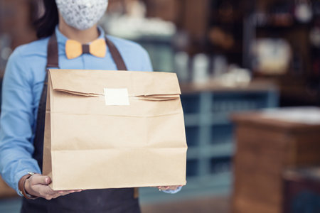 Takeaway food in a paper bag handed over by restaurant waitress as services are limited in their operation.の写真素材