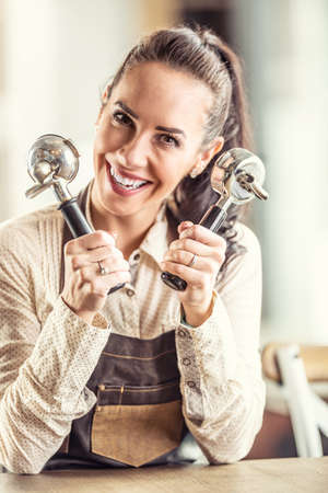 Happy good-looking waitress holds two portafilters in her hands smiling at the camera.の写真素材