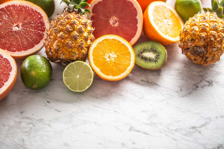 Various citruses such as oranges, limes, grapefruits, as well as pineapples on a marble surface.