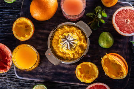 Top view of juicer full of orange pulp with fresh citruses, juices and fruit skins around.
