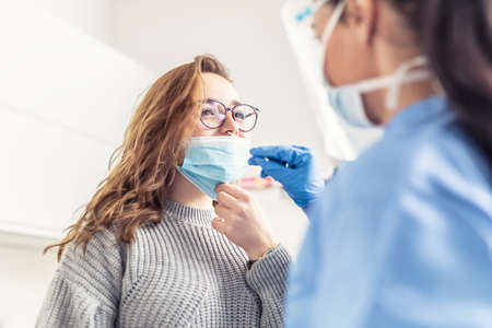 Smiling girl puts face mask off her nose so that a healthcare worker can take a sample for Covid-19 testing.の写真素材