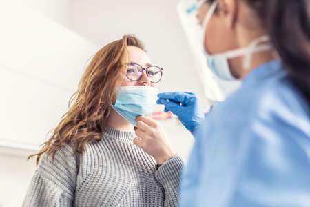 Smiling girl puts face mask off her nose so that a healthcare worker can take a sample for Covid-19 testing.