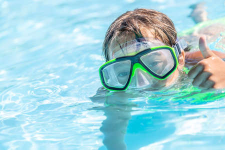 Child swimming in a pool with goggles on showing thumbs up gesture.の写真素材