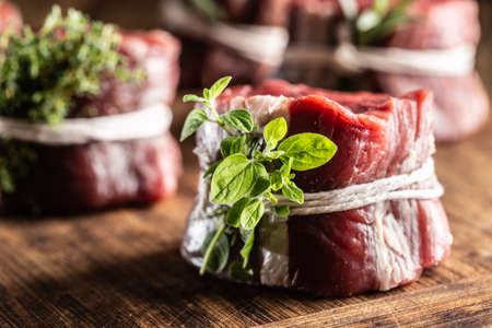 Raw steak wrapped with bacon and fresh thyme on a wooden cutting board.の写真素材