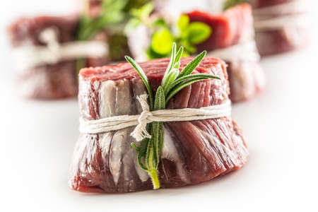 Raw steak wrapped with bacon and fresh thyme on a wooden cutting board.