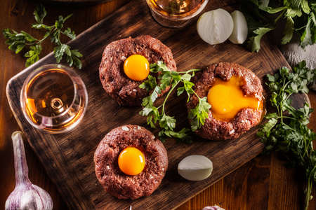 Top view of appetizing beef steak tartare with delicious egg yolk and alcohol. Served on a wooden...