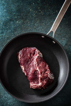 Top view of a dark pan with a raw chunk of steak meat on a marble surface.の写真素材