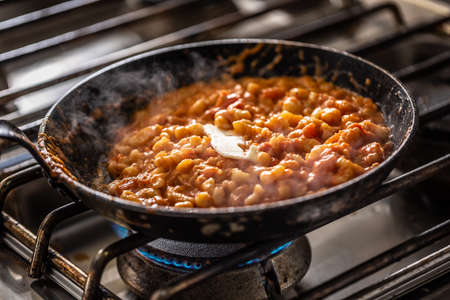 Italian gnocchi in a tomato sauce with a knob of butter melting in a dark pan on a stove.の写真素材