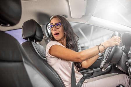 Unexperienced driver with frightened facial expression reverses car looking over her shoulder.