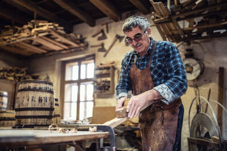 Carpenter in glasses uses jack-plane to smooth the surface of wood in the workshop.の写真素材