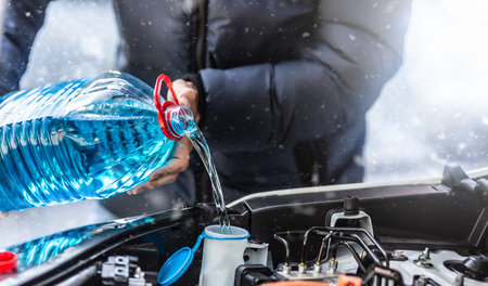 The male driver pours antifreeze into the tank to spray the windshield during a snowstorm.の写真素材