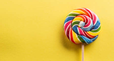 Sweet round lollipop with rainbow colour on the wooden stick with yellow background.の写真素材