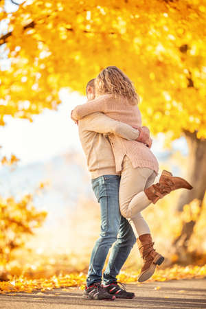A man holds in his arms a woman in an embrace with kisses in the autumn park.の写真素材