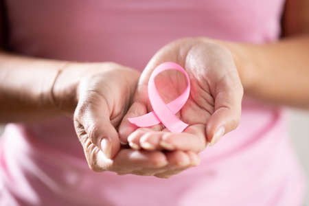 Pink ribbon held in female hands to raise the awareness of necessity for breast cancer prevention.の写真素材