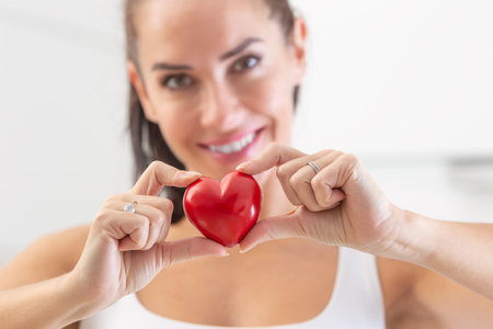 Pretty woman holds a small red heart in her fingers, smiling.の写真素材
