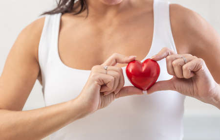 Woman holds small red heart over her chest in the area where the real heart is as a symbol of heart...