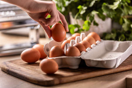 Female hand picks an egg with a carton box lying on the kitchen counter.