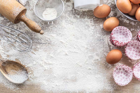 Baking utensils with eggs flour and cupcake cases on kitchen table - Top of view.の写真素材
