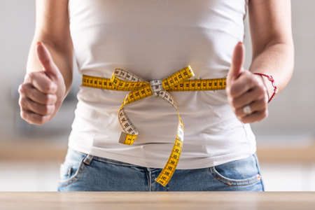Detail of a butter-tied measuring tape around woman's waist with her fingers up.の写真素材
