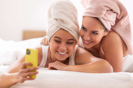 Mom and daughter having wellness time at home wearing towels on their heads, taking selfies.の写真素材