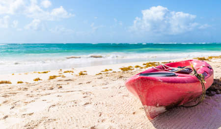 Pink sea kayak parked on a beach on a hot sunny day next to a turquoise blue sea in an exotic travel destination.の写真素材