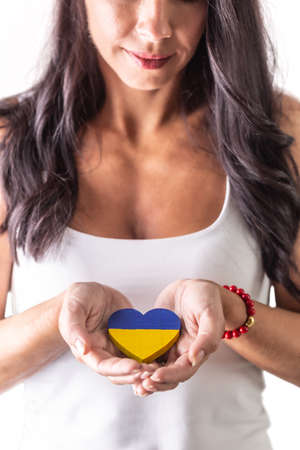 Brunette woman holding a Ukrainian heart carefully in her hands in fron of her chest. Representing love and emphaty to attacked people. Isolated background.の写真素材