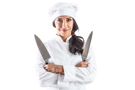 Female cook standing with arms crossed holding two sharp knives - isolated on white.