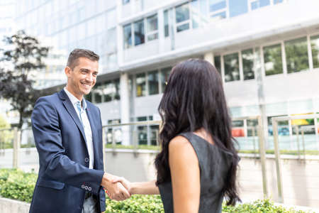 Man and woman dressed in office wear shake hands outdoors in front of an office building.の写真素材