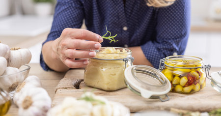 Detail of woman putting a sprig of rosemary on top of a jar full of crushed garlic paste.