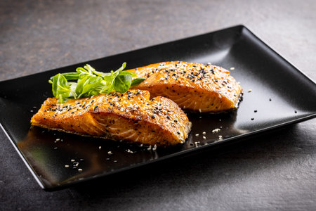 Two salmon fillets baked until crispy, sprinkled with sesame on a black plate.の写真素材