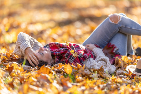 Carefree beautiful brunette lying in the park relaxing during sunny autumn sunset.の写真素材