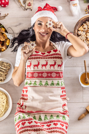 A cheerful cook in a Christmas apron lies on the ground and covers her eyes with cakes, surrounded by traditional holiday dishes and cakes.の写真素材
