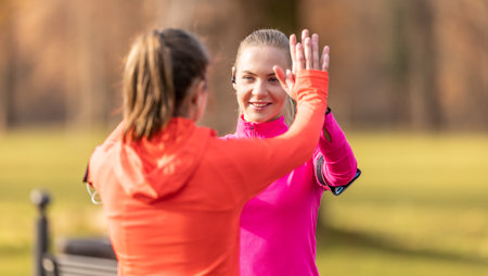 Two female athlete friends support each other and give high-five after a run.