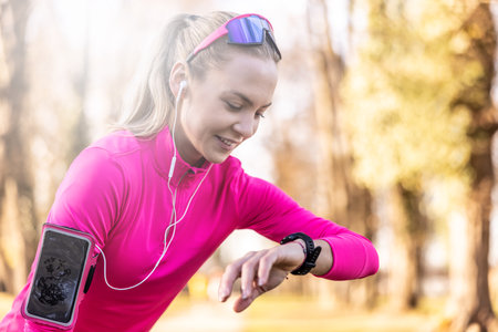 Young woman runner checks her smart watch after running in the park.の写真素材