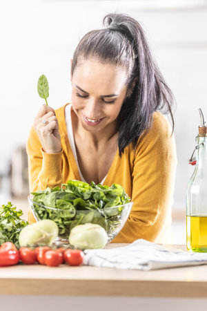 Nice young woman holding a spinach leaf, smiling, fresh vegetables on the table next to her.の写真素材