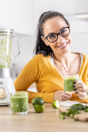 Happy woman with spinach smoothie drink or vegetarian shake sitting in her kitchen.の写真素材
