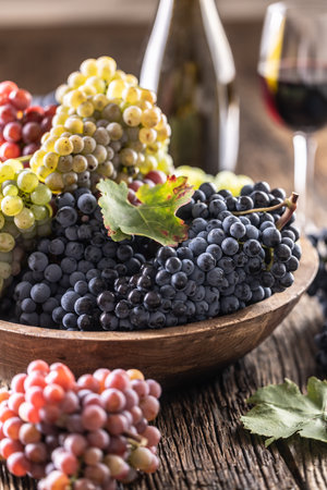 Juicy bunches of grapes in a wooden bowl, red wine in the background.